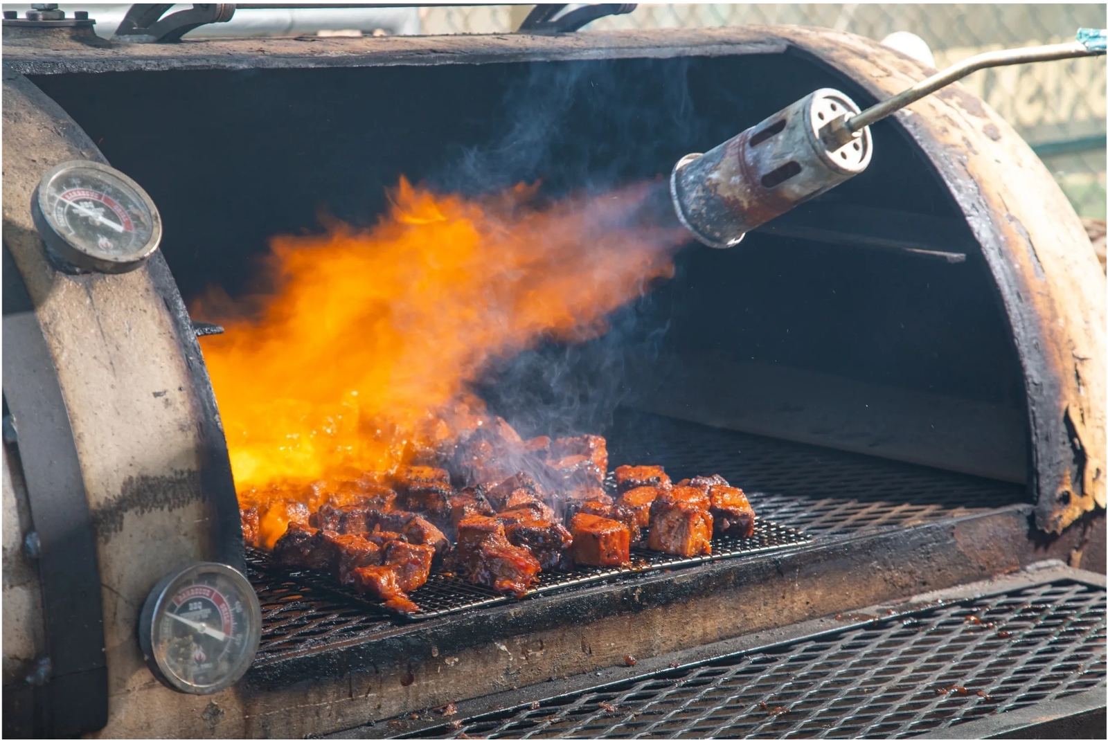 Flames in the open smoker over a grill full of wings